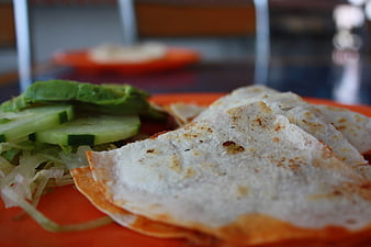 Close-up of quesadilla slices with avocado and cucumber on orange plate
