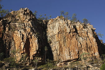 Rugged Sandstone Cliff Face with Sparse Vegetation Under Blue Sky