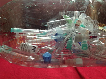 Used medical syringes and needles in clear plastic container on red cloth