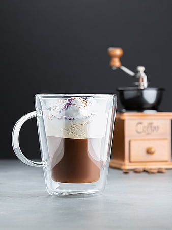 Iced coffee in double-walled glass mug with foam and coffee grinder background