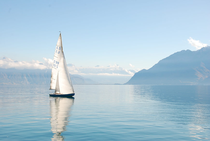 Lone Sailboat on Calm Lake with Mountain Background