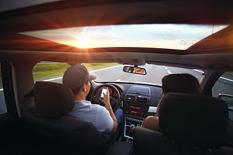 Man Using Smartphone While Driving Car at Sunset