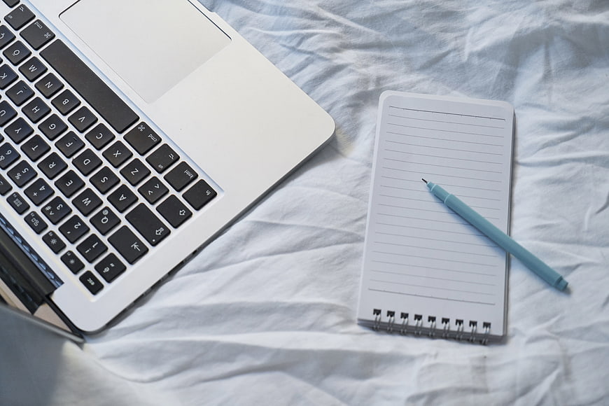 Laptop, Notebook, and Pen on White Bedding