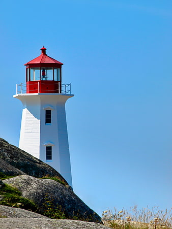 White Lighthouse with Red Roof on Rocky Cliff