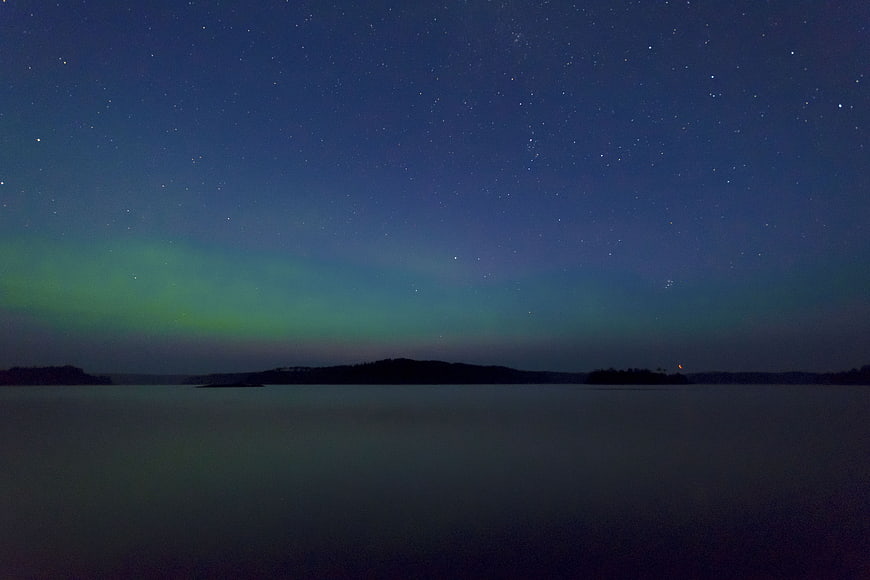 Aurora Borealis over calm lake with starry night sky
