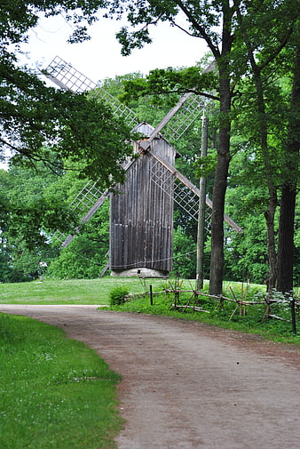 Old wooden windmill in a green park with a dirt path