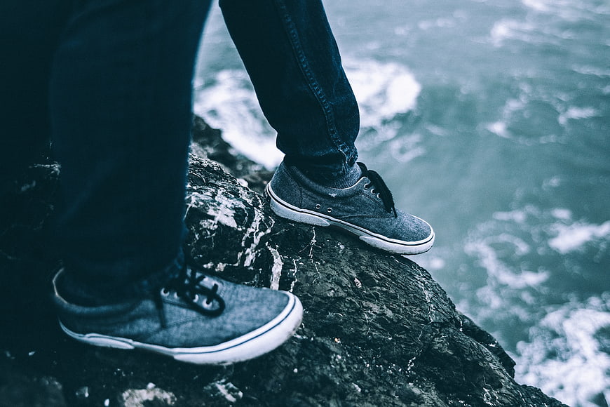 Man standing on rocky cliff edge overlooking ocean waves