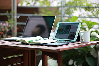 Outdoor workspace with laptop, tablet, notebook, and coffee on wooden table