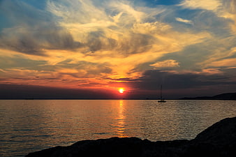 Golden sunset over calm sea with sailboat silhouette and dramatic clouds