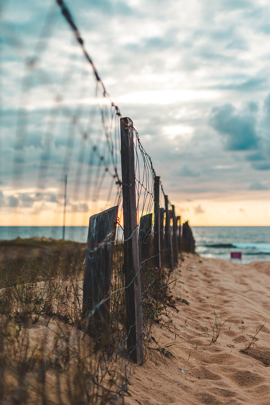 Rustic wooden fence on sandy beach at sunset