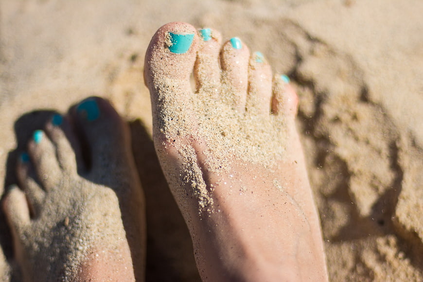 Close-up of feet with turquoise nail polish in sand