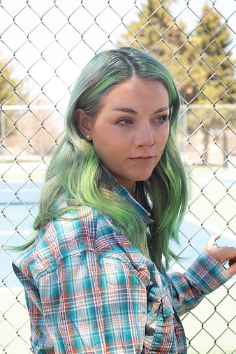 Portrait of young woman with green hair leaning on chain link fence