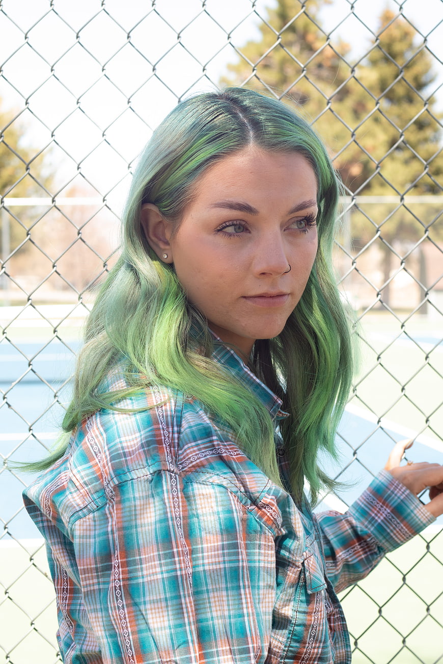 Portrait of young woman with green hair leaning on chain link fence