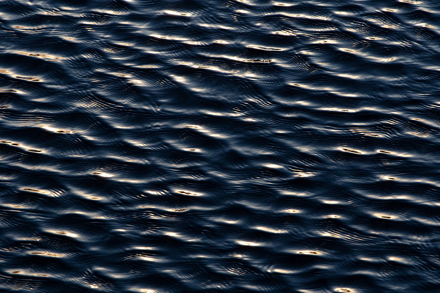 Dark rippling water texture with golden light reflections