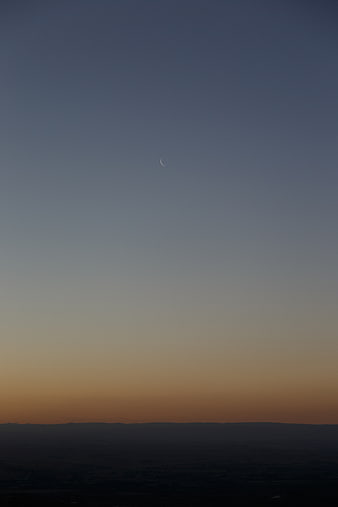 Crescent moon in twilight sky over dark landscape silhouette