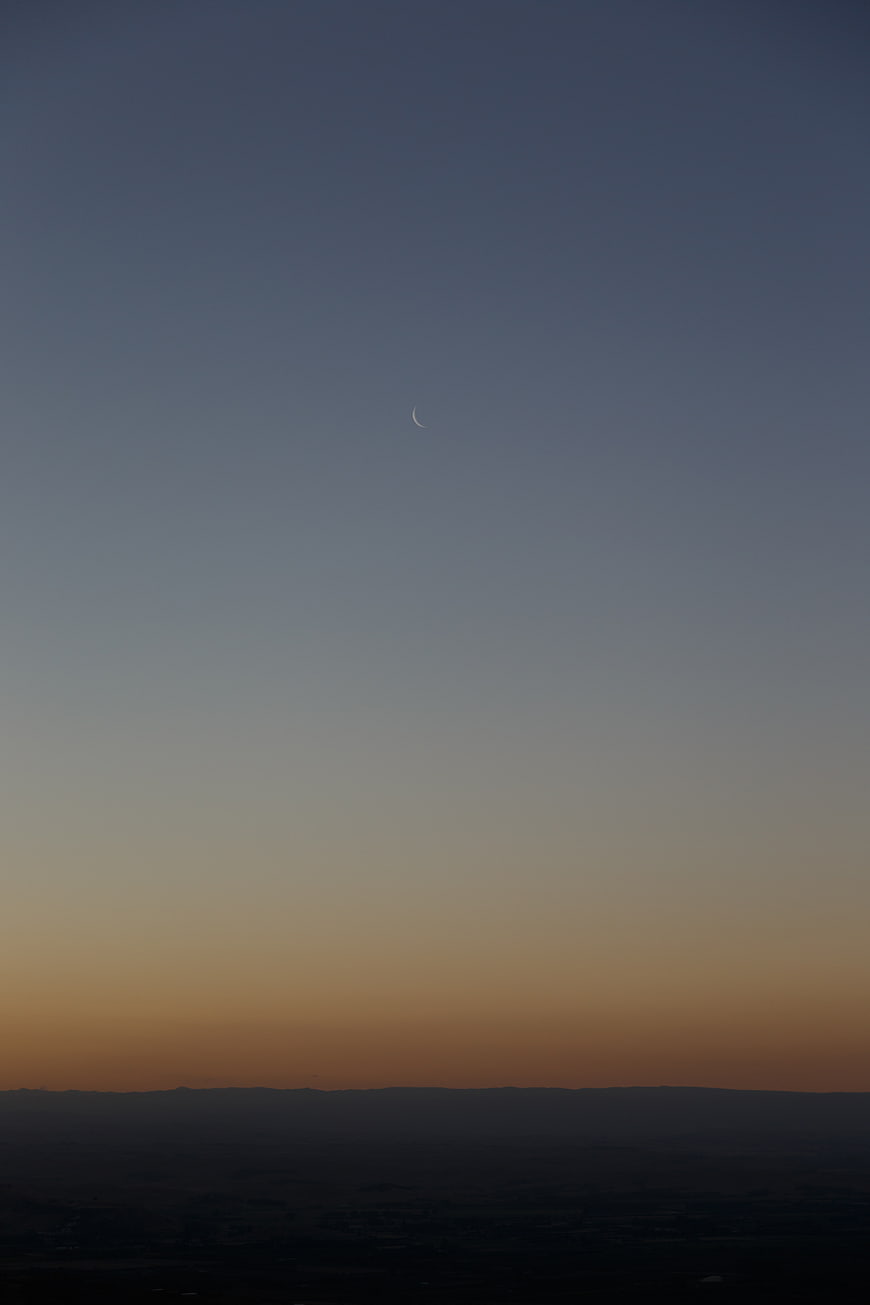 Crescent moon in twilight sky over dark landscape silhouette
