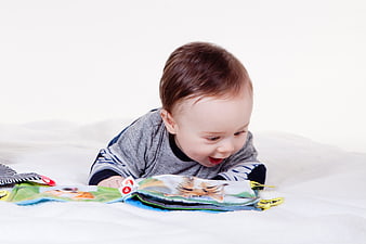 Happy baby lying on white blanket reading colorful picture book
