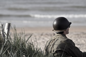 Soldier in WWII uniform sitting on beach looking at ocean