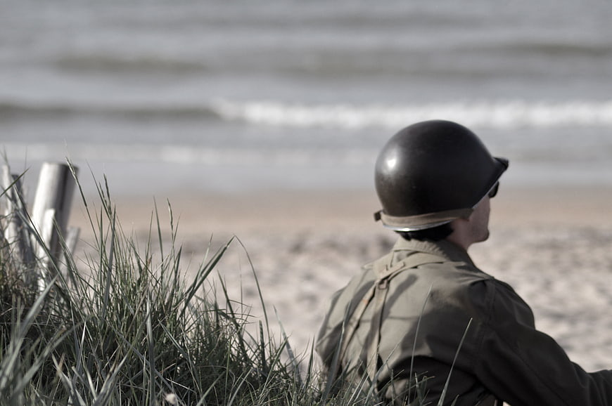 Soldier in WWII uniform sitting on beach looking at ocean