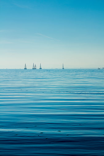 Serene Blue Ocean with Distant Sailboats on Calm Water