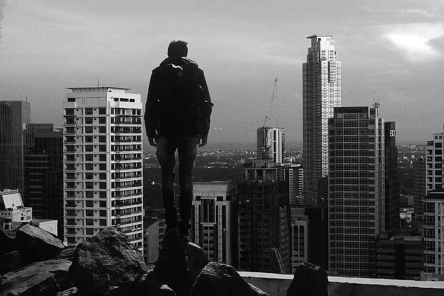 Silhouette of Man Standing on Rocks Overlooking City Skyline