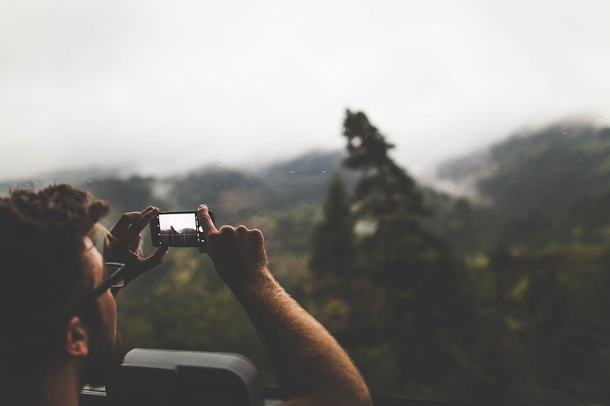 Man taking photo of misty mountain landscape with smartphone