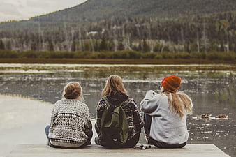 Three women sitting on dock looking at lake