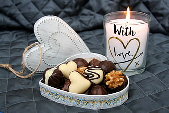 Heart-shaped box of chocolates and lit candle with love text
