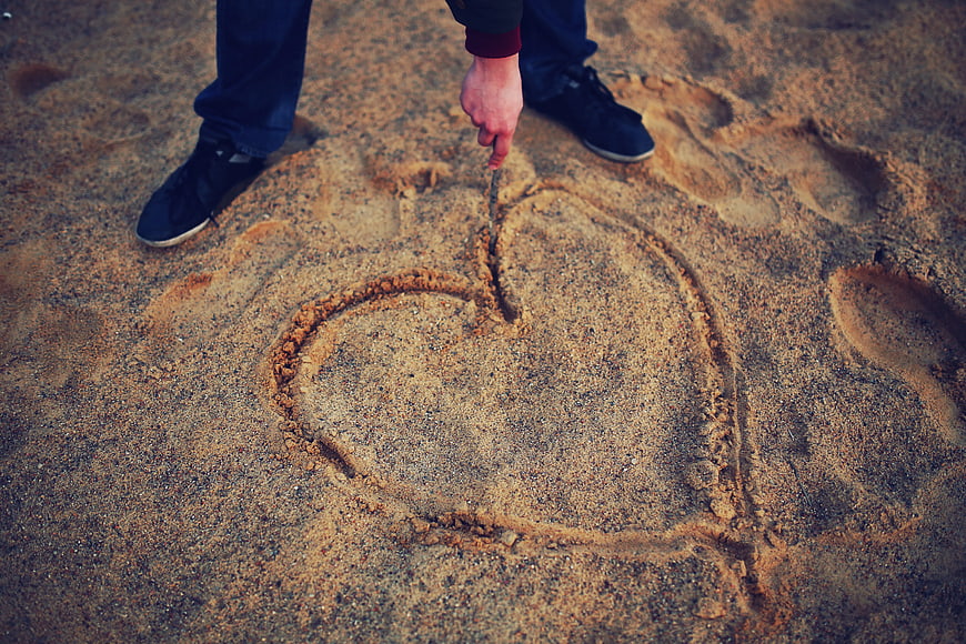 Hand drawing heart in sand with stick