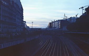 Urban Train Tracks at Dusk with City Buildings and Construction Cranes