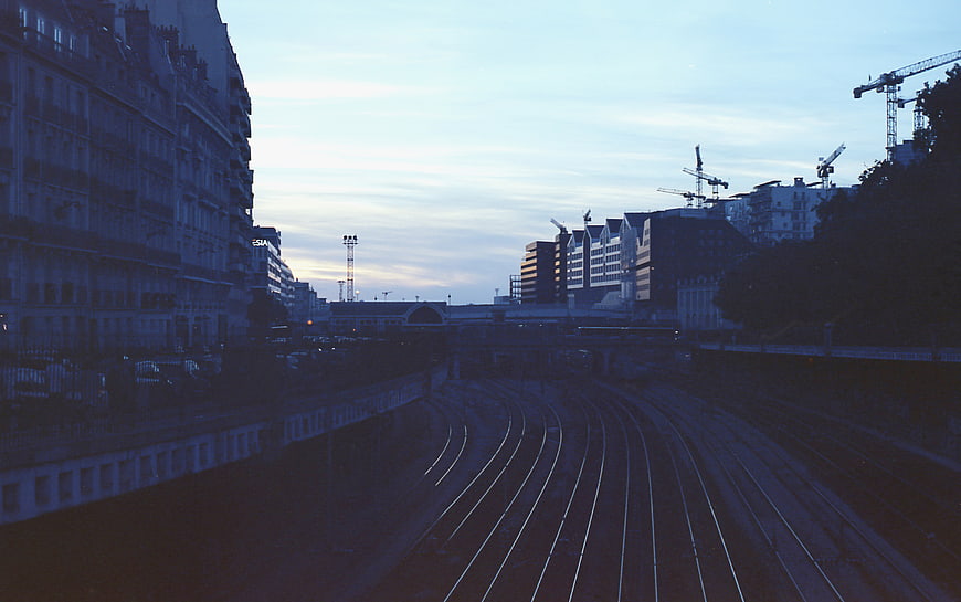 Urban Train Tracks at Dusk with City Buildings and Construction Cranes