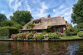 Traditional Dutch Thatched Cottage With Vibrant Garden By Canal