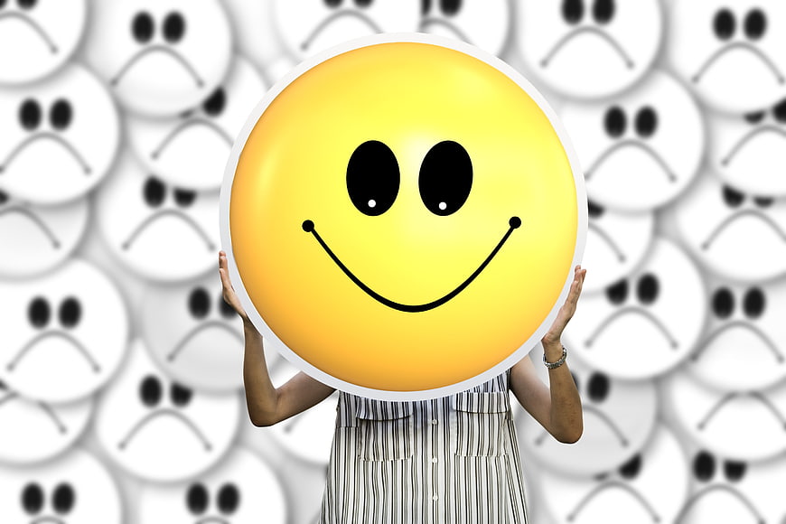 Person holding large yellow smiley face against background of sad faces
