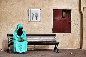 Woman in teal abaya and niqab sitting on a wooden bench