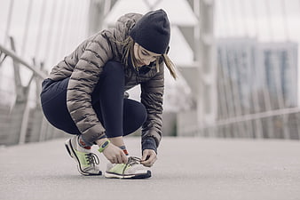 Woman tying running shoes on bridge in winter