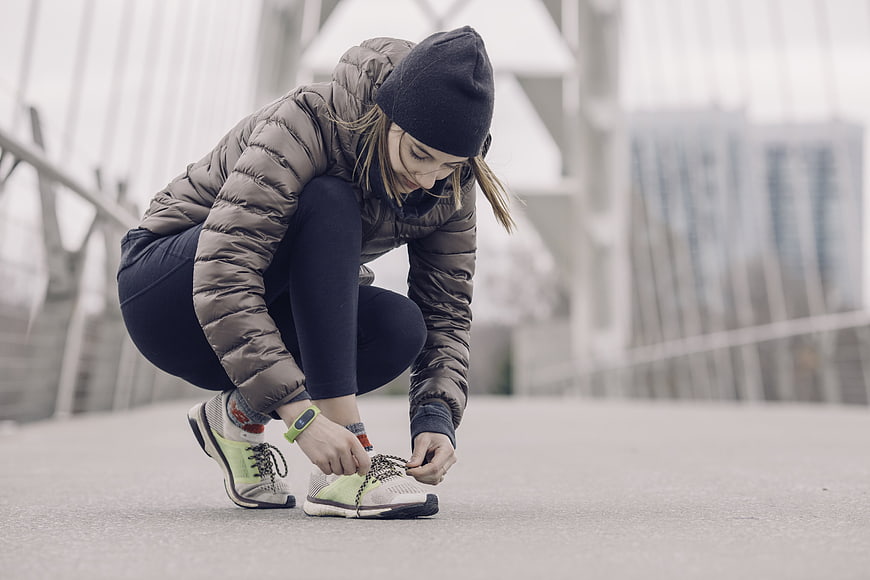Woman tying running shoes on bridge in winter