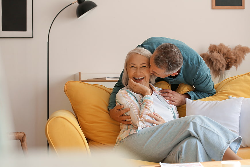 Happy Senior Couple Laughing on Yellow Sofa at Home