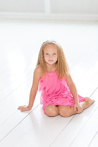 Cute little girl in pink dress sitting on white floor