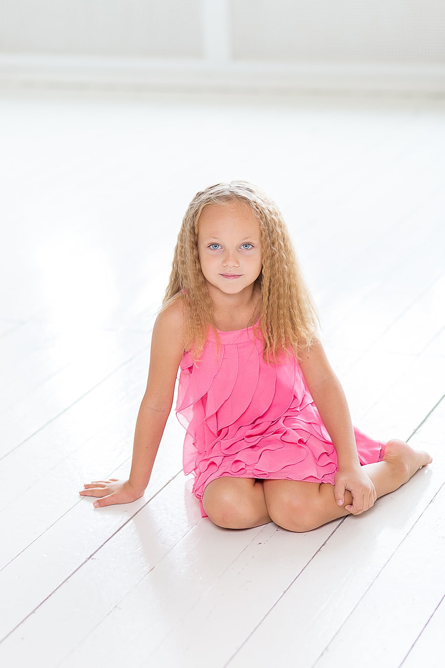 Cute little girl in pink dress sitting on white floor
