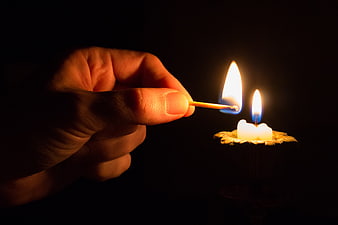Hand Lighting Candle with Match in Darkness