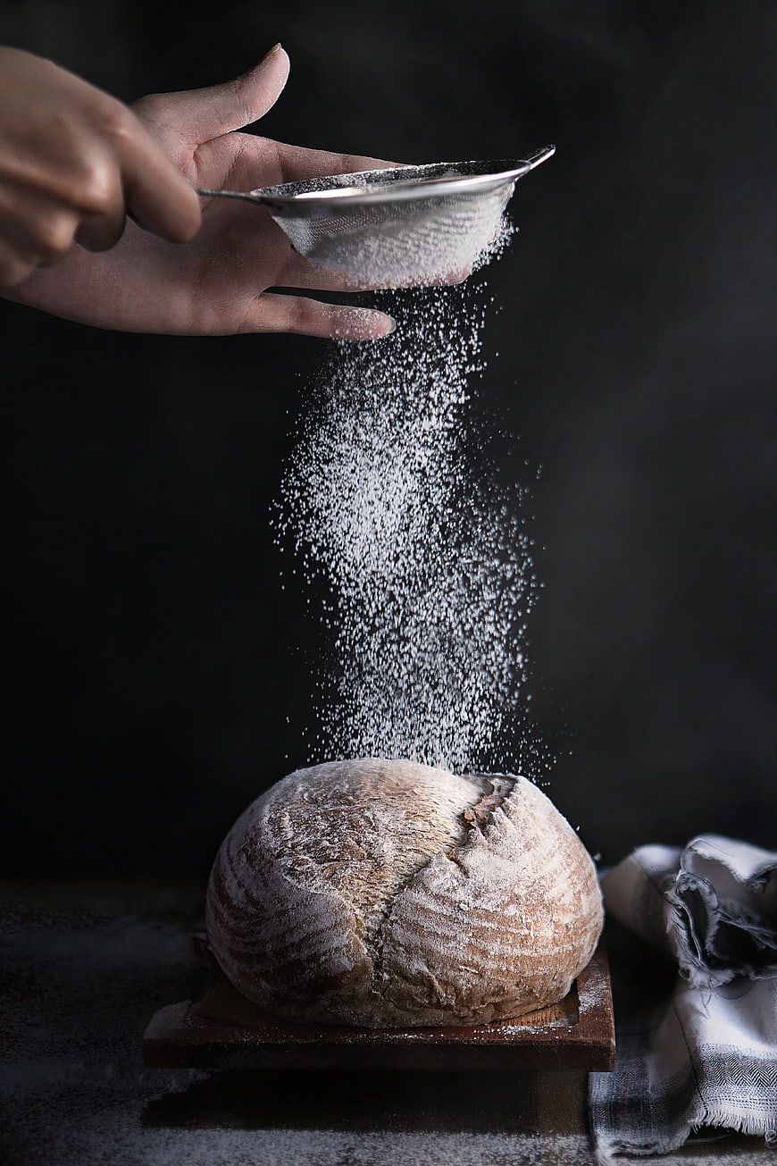 Hand Sifting Flour Over Rustic Artisan Bread Loaf