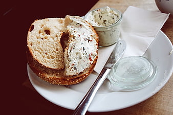 Sesame bagel with herb cream cheese on white plate