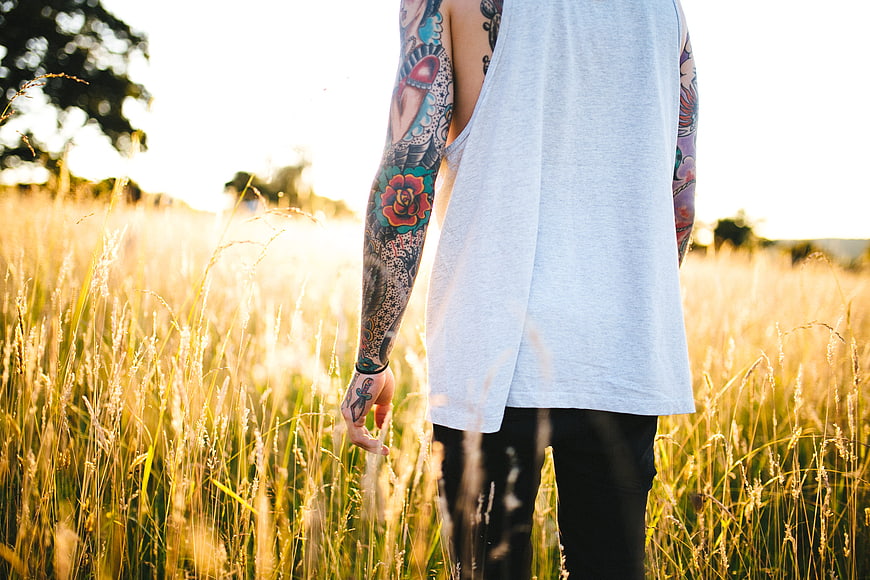 Man with Colorful Tattoos Walking Through Golden Grass Field