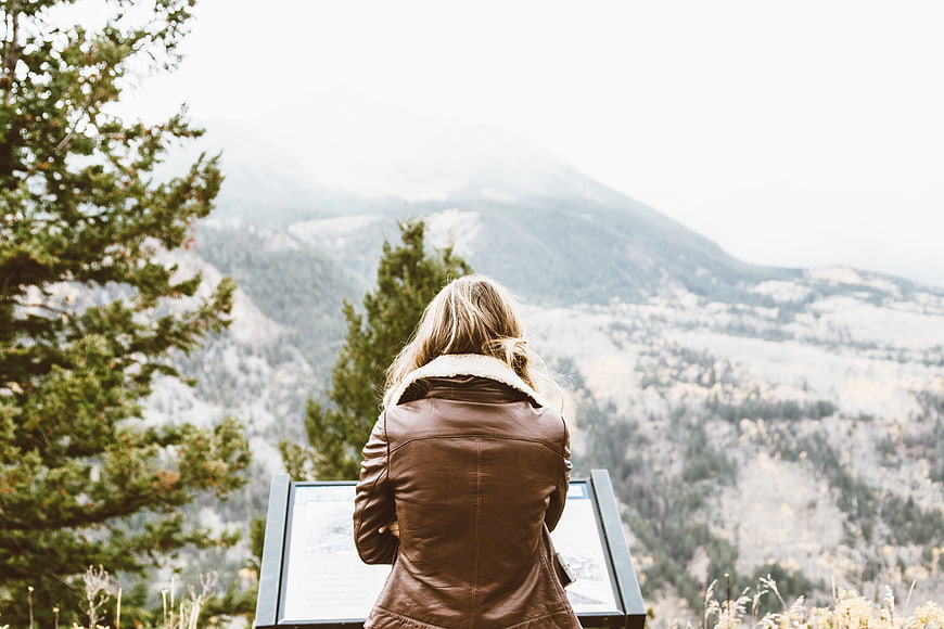 Woman in brown leather jacket viewing mountain landscape