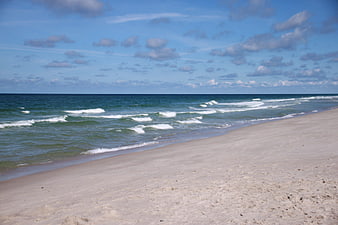 Sandy beach shoreline with blue ocean waves and cloudy sky