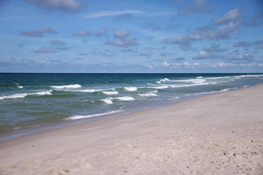 Sandy beach shoreline with blue ocean waves and cloudy sky