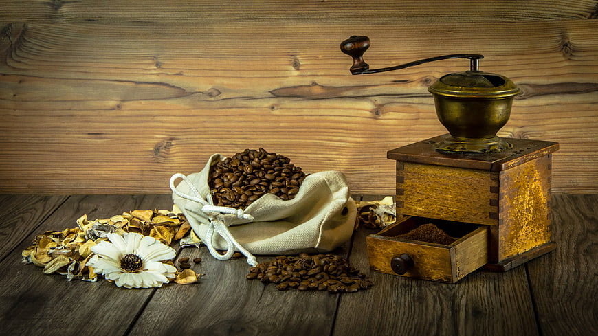 Vintage coffee grinder and raw beans in burlap sack on rustic wood table
