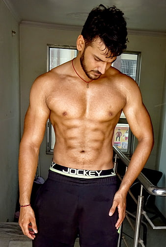 Muscular shirtless man with defined abs and chest in indoor setting