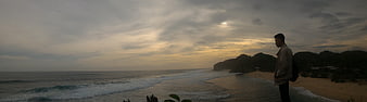 Man standing on beach looking at ocean sunset