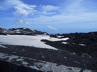 Snowy volcanic landscape with black lava rocks and blue sky